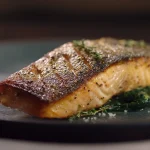 A close-up serving of Gordon Ramsay's pan-fried salmon on a bed of spinach, highlighting the crispy skin and moist flesh.